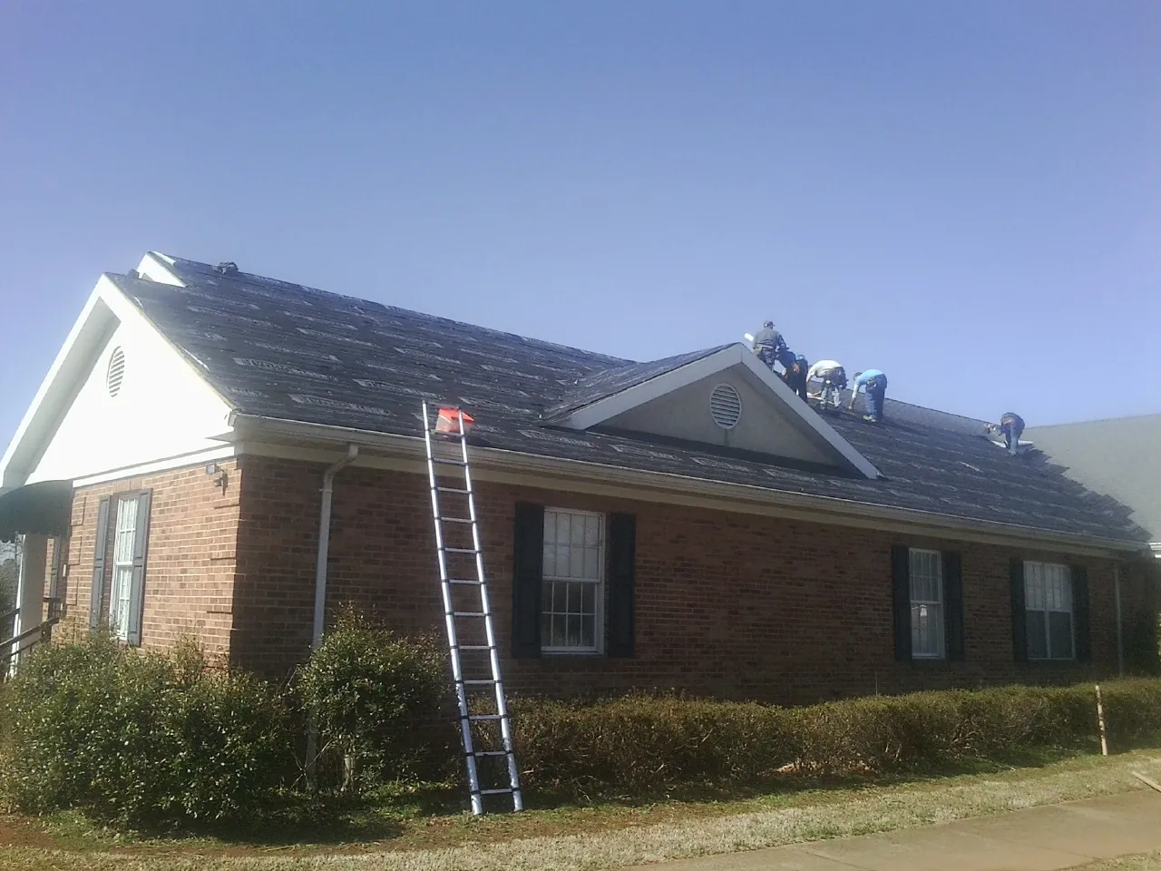 Crew tearing shingles off a brick ranch roof with a ladder set — Emergency Roof Repair work by our crew in Anna