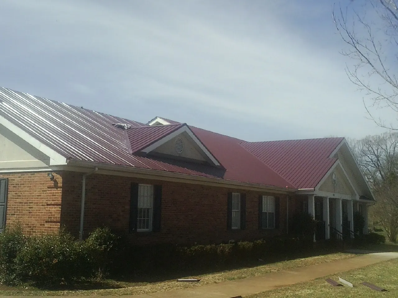 Red metal roof with gabled entries on a long brick building, from a Hail Damage Roof Repair job in Anna